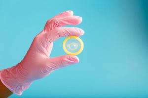 Condom contraception A hand in a pink glove holds a condom on a blue background. Latex for semen and protection against pregnancy. photo