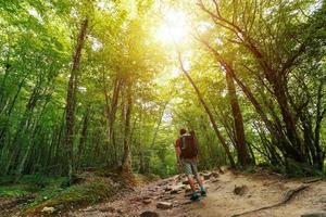 A traveler with a backpack in the spring forest on the path looks ahead. Sunlight through the crowns of trees. photo