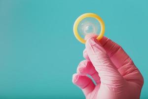 un condón abierto en una mano con un guante rosa se sostiene sobre un fondo azul. látex para la protección contra el embarazo. foto