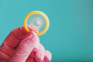 An opened condom in a hand in a pink glove holds on a blue background. Latex for protection against pregnancy. photo