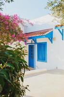 Traditional white greek house with blue windows and doors, pink flowers photo