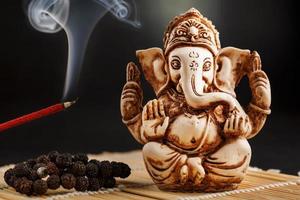 Ganesha on a black background. Statue and rosary with red smoldering incense stick photo