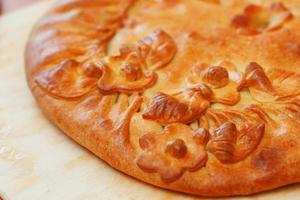 Russian pie with potatoes and mushrooms on the table. Freshly baked big cake decorated with flowers of their dough photo