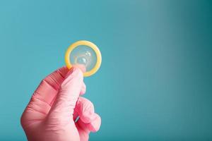 anticoncepción del condón una mano en un guante rosa sostiene un condón sobre un fondo azul. látex para semen y protección contra el embarazo. foto