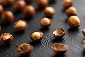 Purified and shell repeats macadamia nuts on black textural stone background. Healthy eating concept photo