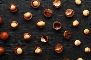 Purified and shell repeats macadamia nuts on black textural stone background. Healthy eating concept photo