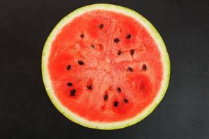 Half of tasty and ripe red watermelon on a black background, texture of juicy pulp of ripe red watermelon with seeds photo