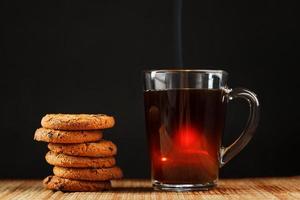 Oatmeal cookies with pieces of chocolate and a mug of coffee on a bamboo stand. photo