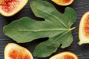 Juicy Figs on a dark background and a large leaf, pulp of fig slices with seeds close-up. The fig fruit is purple, a green leaf, on a black substrate with a dark background. photo