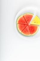 Pieces of red and yellow watermelon in a white round plate, on a white background. View from above. A slice of red watermelon is one among the yellow pieces. Highlight photo