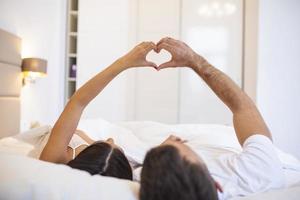 Couple Lying On Bed Forming Heart Shape With Hand photo