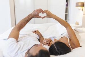 pareja acostada en la cama formando forma de corazón con la mano foto