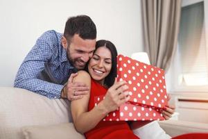 Young couple at home holding a present. Man suprising his wife with gift box on Valentines day. photo