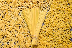 Raw pasta various kinds of uncooked pasta macaroni spaghetti and noodles on background - top view, Italian food culinary concept, Collection of different raw pasta on cooking table for cooking food photo