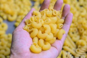 Pasta on hand and raw macaroni background, close up raw macaroni pasta uncooked delicious pasta for cooking food photo