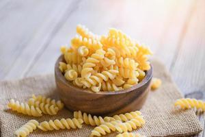 Pasta raw macaroni on wooden bowl background, close up raw macaroni spiral pasta uncooked delicious fusilli pasta for cooking food photo