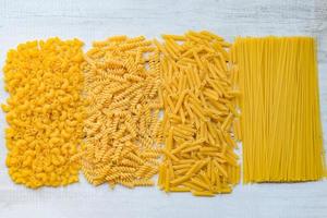 Raw pasta various kinds of uncooked pasta macaroni spaghetti and noodles on background - top view, Italian food culinary concept, Collection of different raw pasta on cooking table for cooking food photo