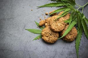 Concepto de hierba de naturaleza de comida de cannabis, galletas de chocolate con hoja de cannabis - planta de hojas de marihuana sobre fondo oscuro foto