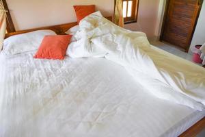 Unmade bed sheet of the crease and pillow white blanket in the bedroom after sleep on top view - Wrinkled fabric sunlight in the morning bed photo