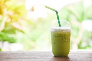 batido de té verde - té verde matcha con leche en vidrio de plástico sobre la mesa de madera y fondo verde natural foto