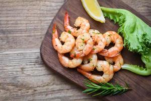 mariscos con romero limón y lechuga - ensalada de camarones a la parrilla deliciosos condimentos especias sobre fondo de tabla de cortar de madera apetitosos camarones cocidos langostinos al horno foto