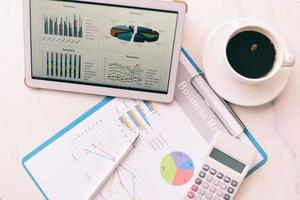 gráfico de gráficos de negocios en una tecnología de computadora de tableta en la mesa con taza de café en el escritorio y calculadora - informe de venta análisis de dinero foto