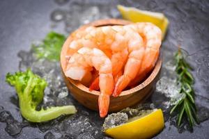 Boiled shrimps prawns on ice frozen at the seafood restaurant fresh shrimp on dark plate with lemon rosemary ingredients herb and spices for cooking seafood photo