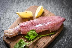 calamares frescos pulpo o sepia para restaurante de ensalada de comida cocinada - calamar crudo en tabla de cortar de madera con perejil de limón en el mercado de mariscos de plato oscuro foto