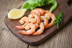 Ensalada de camarones a la parrilla deliciosas especias condimentadas sobre fondo de tabla de cortar de madera apetitosos camarones cocidos gambas al horno, mariscos con romero, limón y lechuga foto