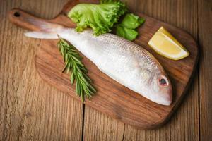 pescado crudo fresco con ingredientes limón romero y lechuga para hacer comida cocinada en tabla de cortar de madera - besugo marisco pescado congelado