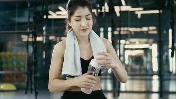 sportig skön kvinna utövar koppla av och dryck vatten med Träning Utrustning suddigt bakgrund, friska liv och Gym övning utrustning och sporter begrepp video