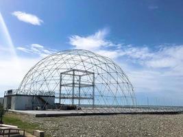 construcción abstracta redonda esférica metal blanco de triángulos en una playa de arena contra el mar y el cielo azul foto