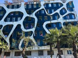 Unusual abstract modern structure white and blue in futuristic style concrete of lines and holes, building, unusual architecture, house with green palm trees. Georgia, Batumi, April 17, 2019 photo
