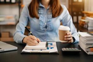 businesswoman hand writing on the notepad with new modern computer strategy diagram and holding coffee cup as concept morning light photo