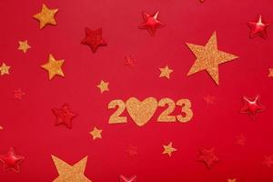 2023 new year flat lay concept. Numbers 2023 with red and gold stars, top view on red background photo