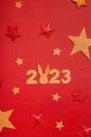 2023 new year flat lay creative concept. Numbers 2023 with rabbit ears, red and gold stars, top view on red background photo