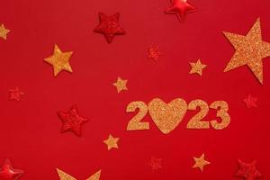 2023 new year flat lay concept. Numbers 2023 with red and gold stars, top view on red background photo