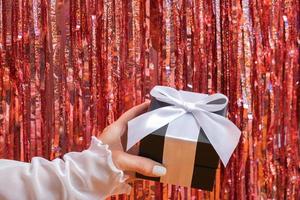 feliz navidad y feliz año nuevo concepto con mano femenina con caja de regalo en el fondo de la fiesta foto