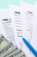 Tax forms lies near hundred dollar bills and blue pen on a light blue background. Income tax return photo