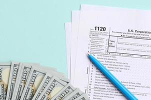 1120 tax form lies near hundred dollar bills and blue pen on a light blue background. US Corporation income tax return photo