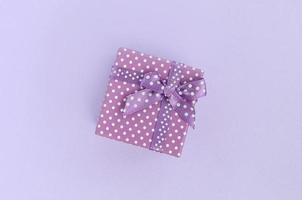 Small purple gift box with ribbon lies on a violet background. Minimalism flat lay top view photo