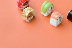 diferentes tipos de rollos de sushi asiáticos sobre fondo naranja. minimalismo vista superior plana con comida japonesa foto