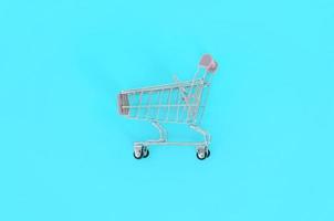 Shopping addiction, shopping lover or shopaholic concept. Small empty shopping cart lies on a pastel colored paper background. Flat lay minimal composition, top view photo