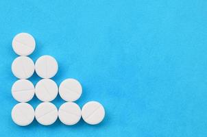 Several white tablets lie on a bright blue background in the form of a triangular arrow. Background image on medicine and pharmaceutical topics photo