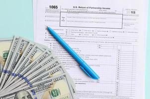 1065 tax form lies near hundred dollar bills and blue pen on a light blue background. US Return for parentship income photo