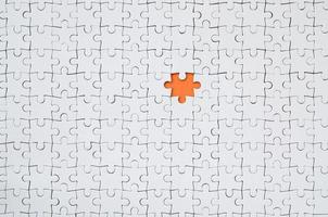 The texture of a white jigsaw puzzle in an assembled state with one missing element forming an orange space photo