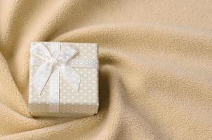 A small gift box in orange with a small bow lies on a blanket of soft and furry light orange fleece fabric with a lot of relief folds. Packing for a gift to your lovely girlfriend photo