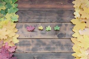algunas de las hojas de otoño caídas amarillentas de diferentes colores en la superficie de fondo de tablas de madera natural de color marrón oscuro foto