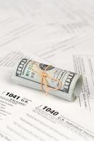 Tax forms lies near roll of hundred dollar bills. Income tax return photo