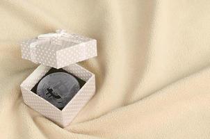 The silver bitcoin lies in a small orange gift box with a small bow on a blanket made of soft and fluffy light orange fleece fabric with a large number of relief folds photo